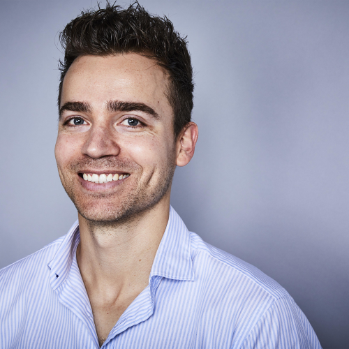 Portrait of Lyndon Galea, who is wearing a pale blue collared shirt in front of a grey background.